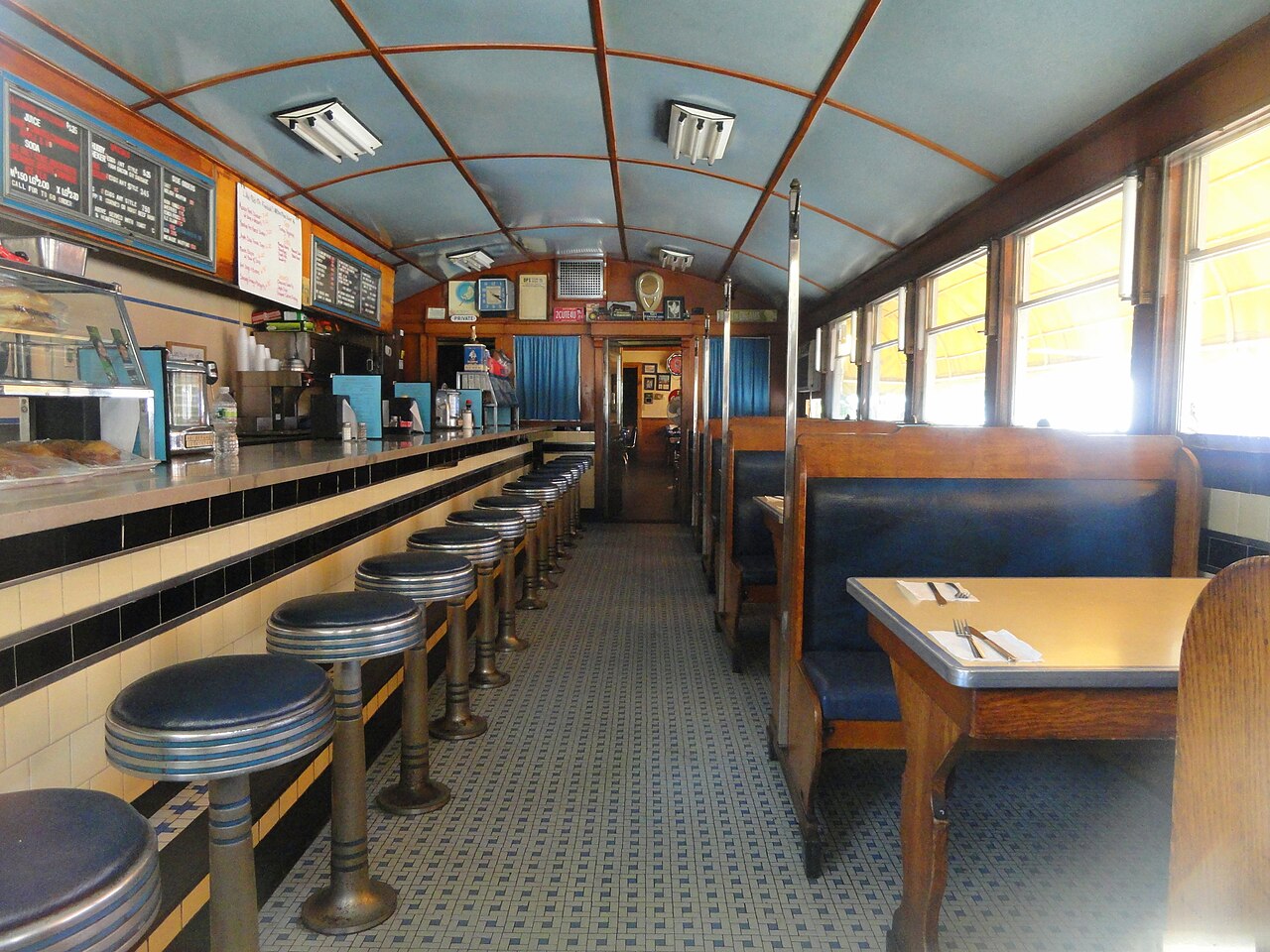 The interior of a classic American diner, with a long counter and stools on one side and cushioned booths on the other