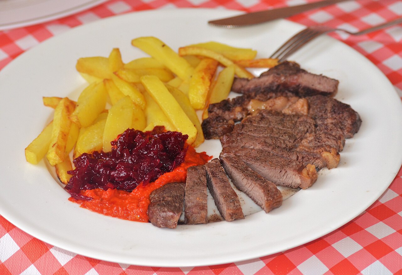 A plated main course (an entree in American English): sliced steak served with a side of fries