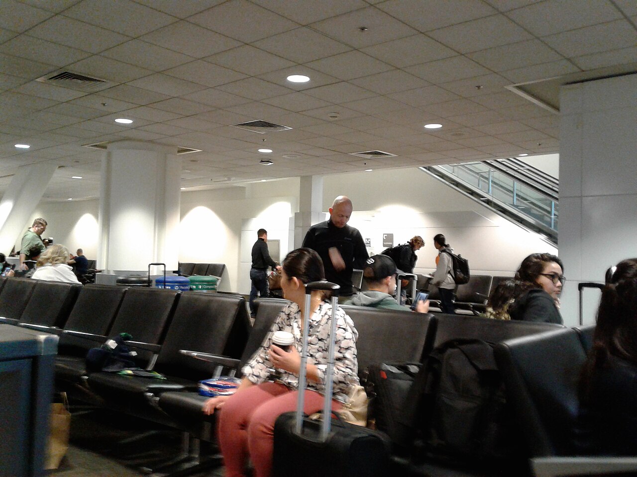 Travelers waiting with their carry-on bags in the seating area at a departure gate
