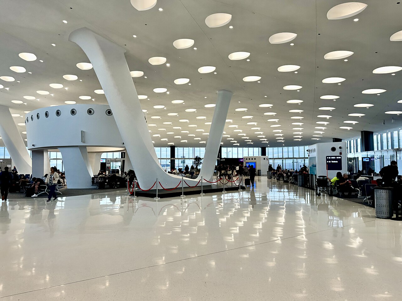 A bright, modern American airport concourse (Chicago O'Hare Terminal 5) with gate seating areas, tall windows and travelers