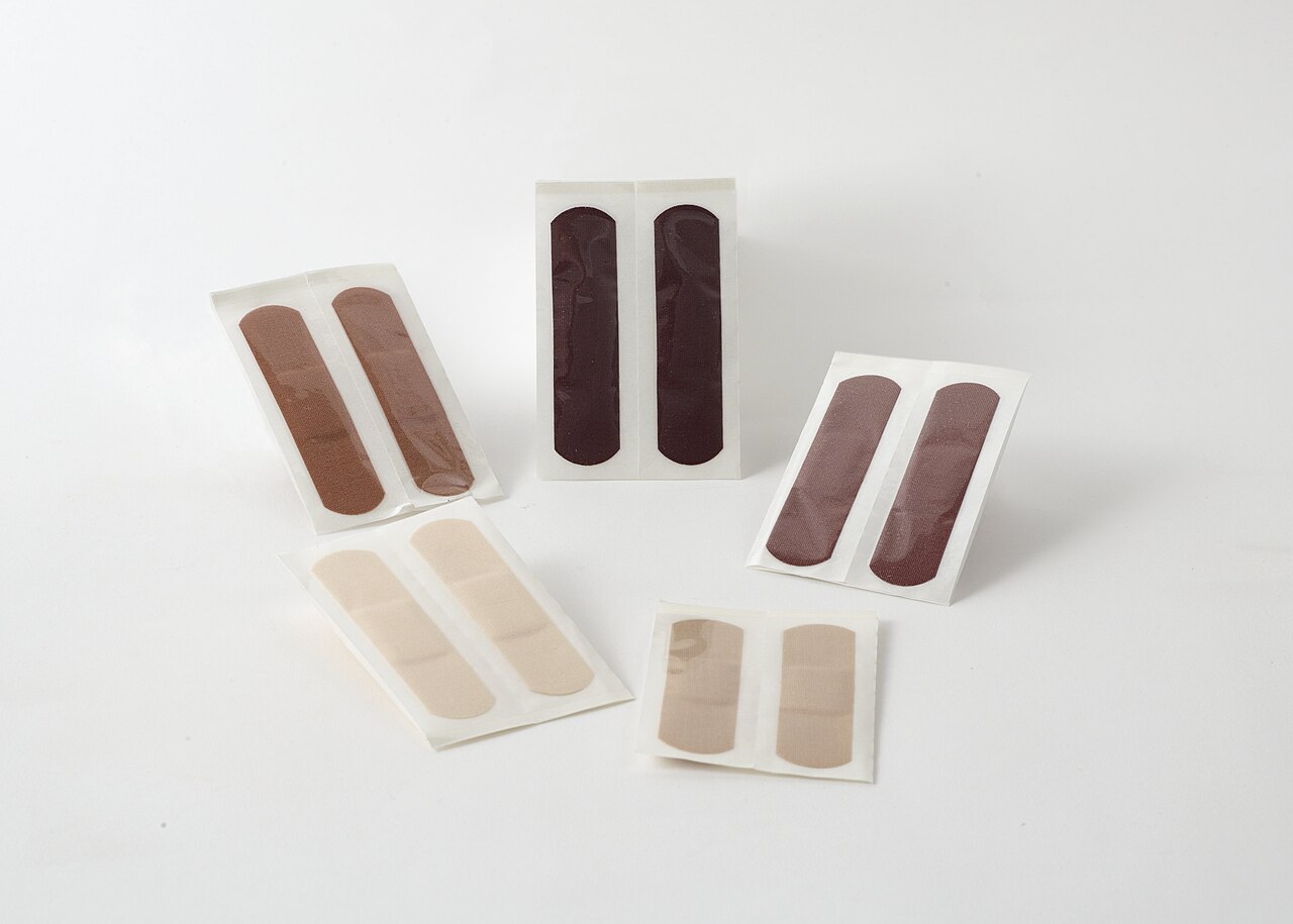 Adhesive bandages in several skin-tone shades on a white background
