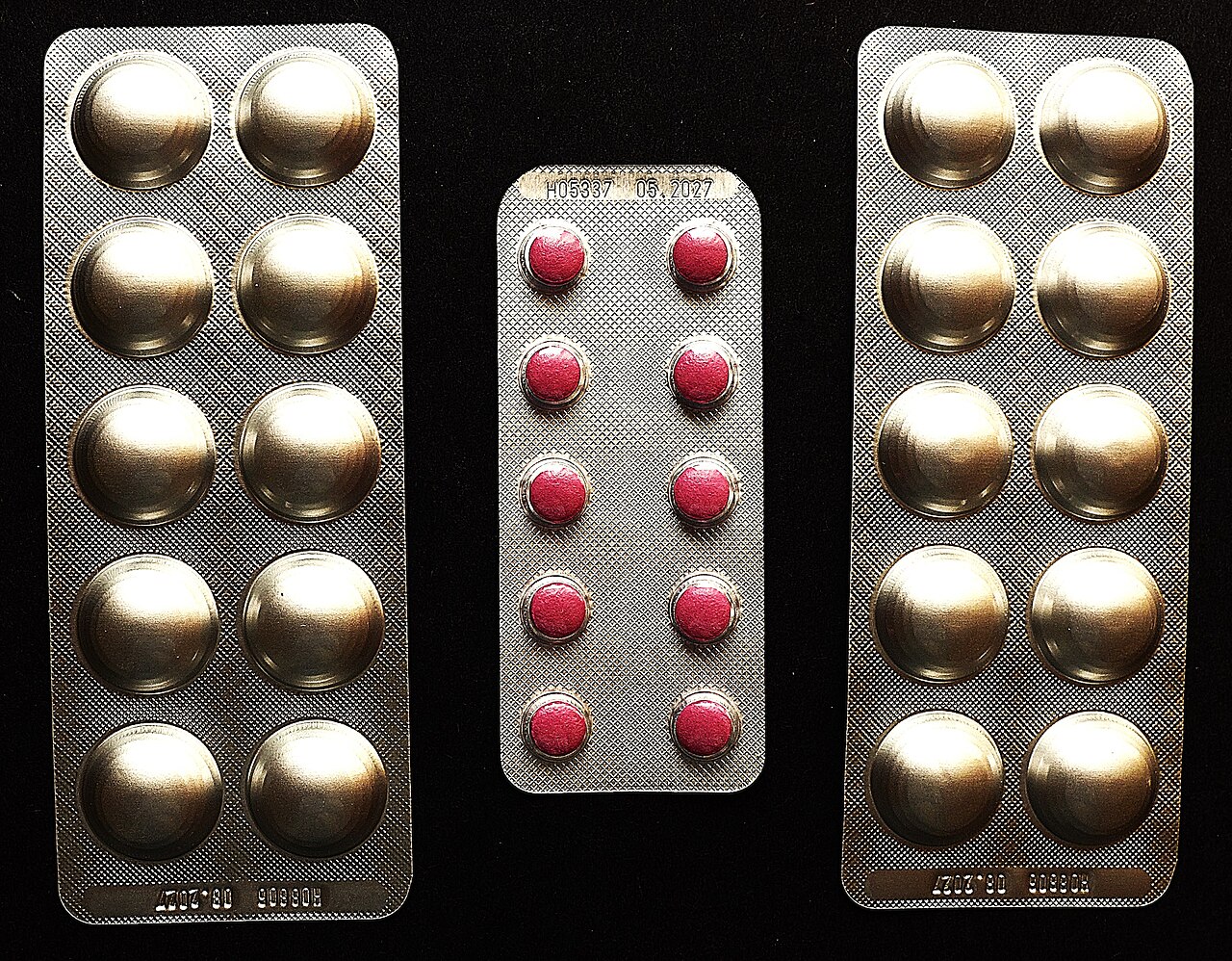 Blister packs of tablets, one with red pills and two with foil-covered pills