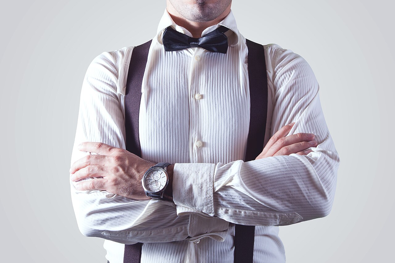 A man wearing dark suspenders and a bow tie over a white dress shirt