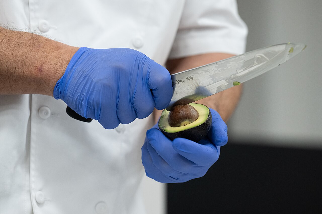 A chef slicing an avocado with a large kitchen knife