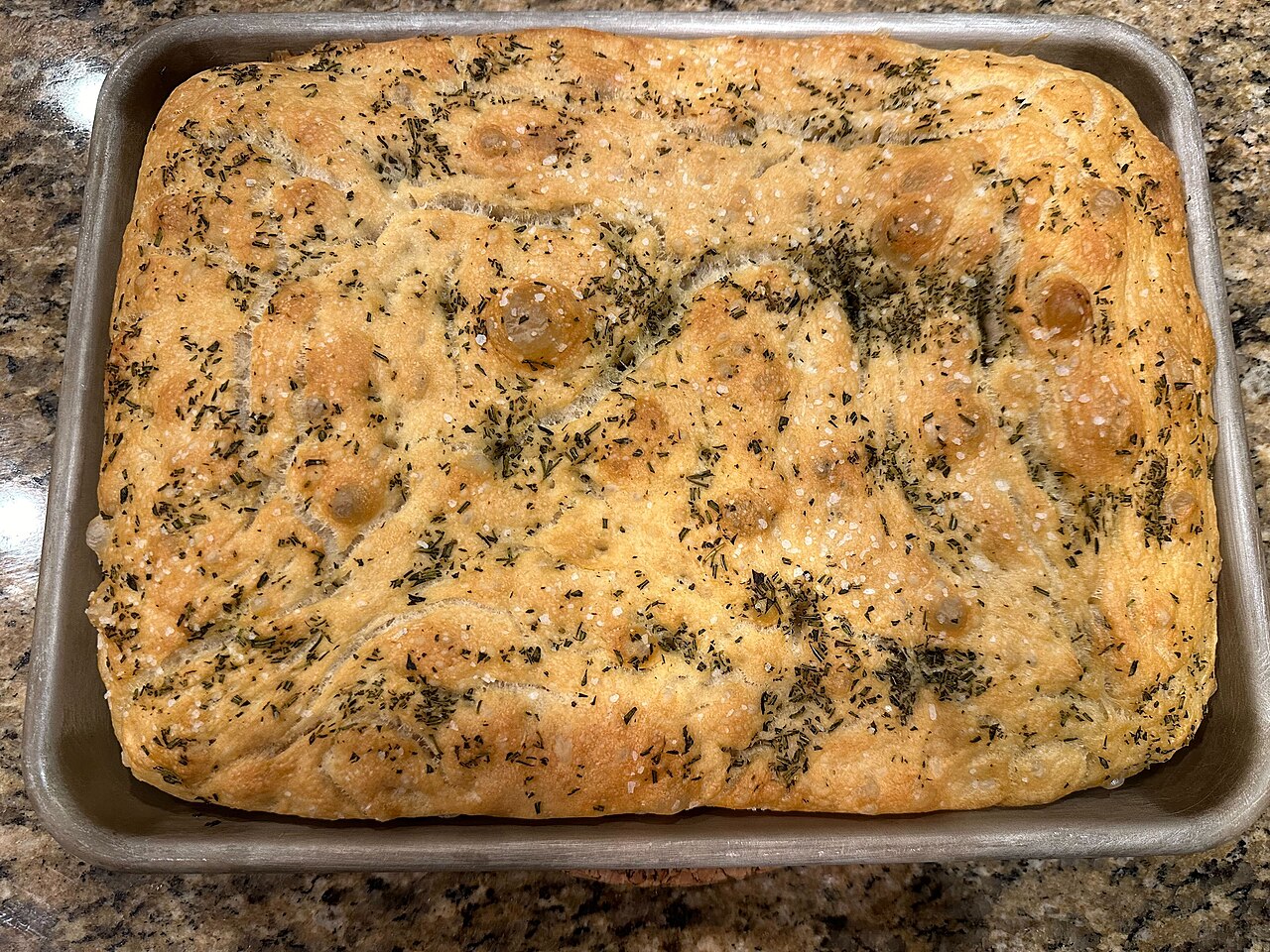 A freshly baked rosemary focaccia in a metal baking pan
