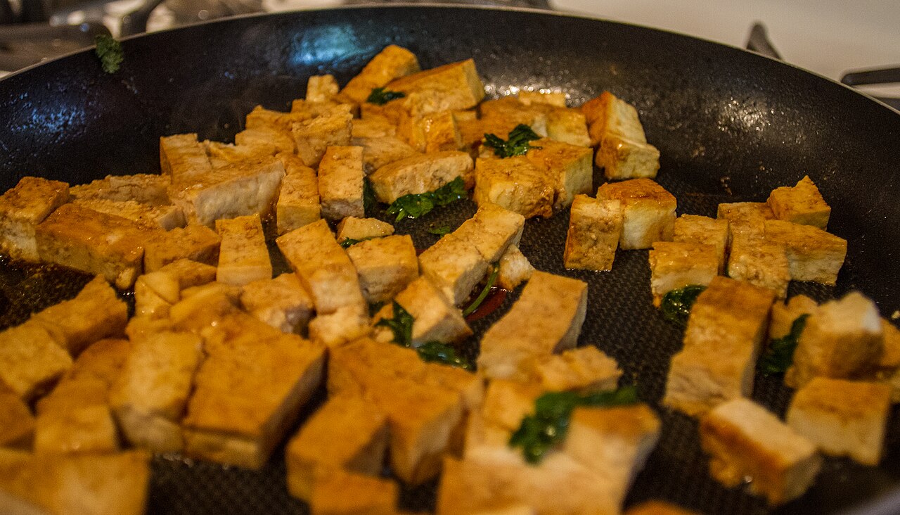 Cubes of tofu frying and sizzling in a large pan