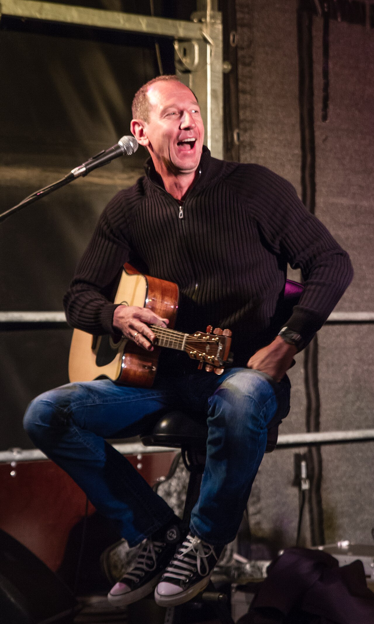 A musician laughing with delight while playing a guitar on stage