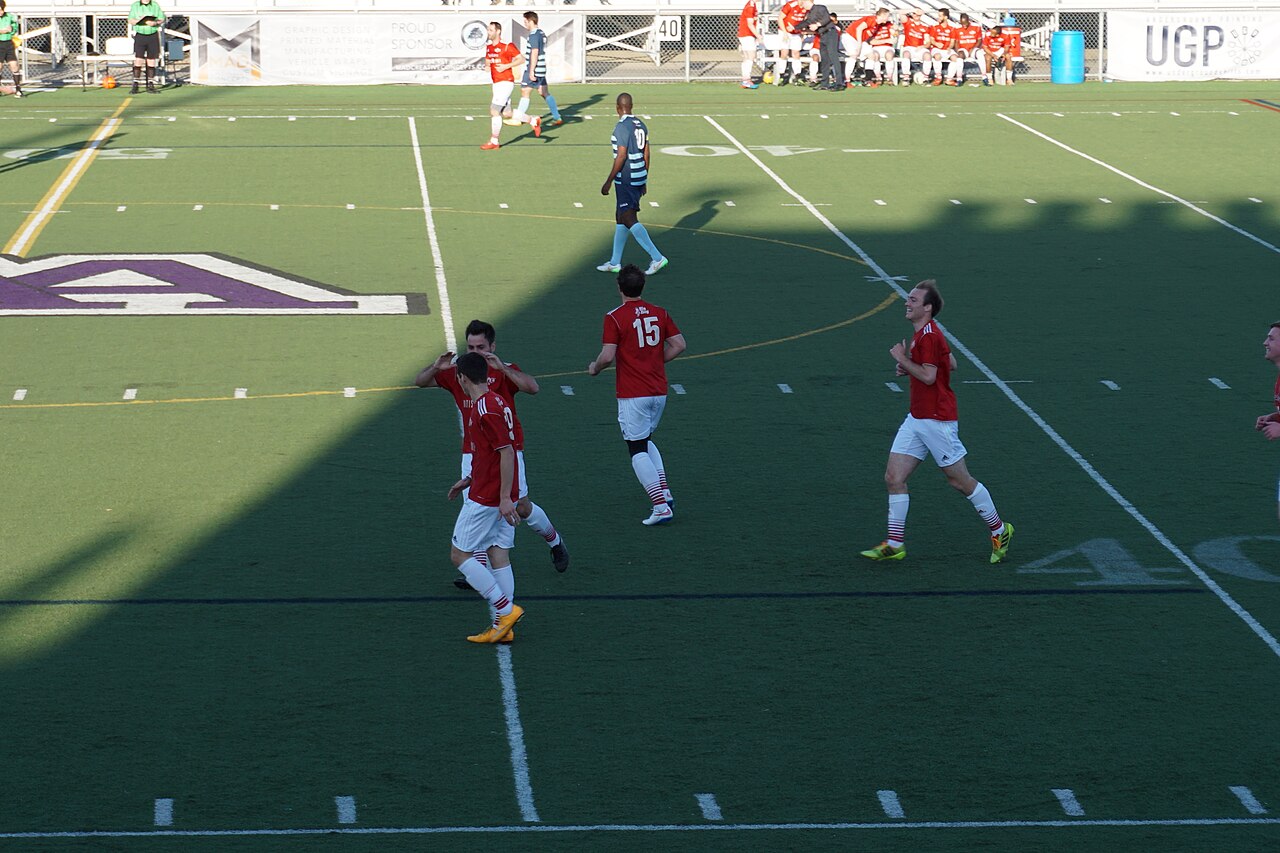Forwards in red celebrating together after scoring a goal
