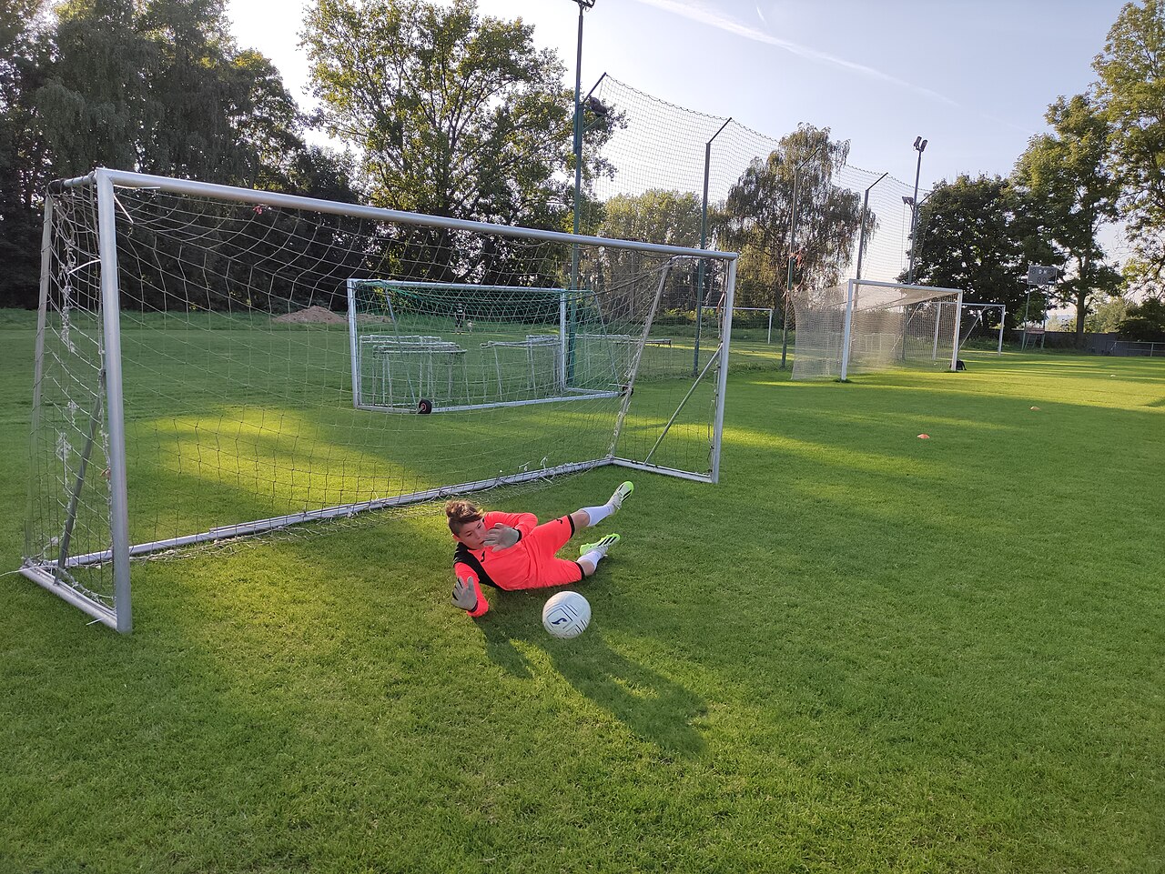 A goalkeeper in a bright kit diving to stop the ball in front of the goal