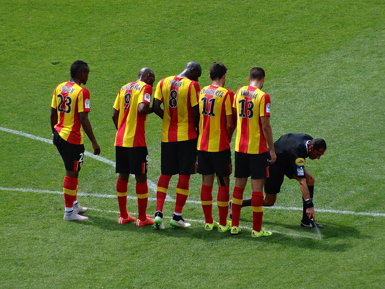 The referee, dressed in black, marking the line in front of a defensive wall