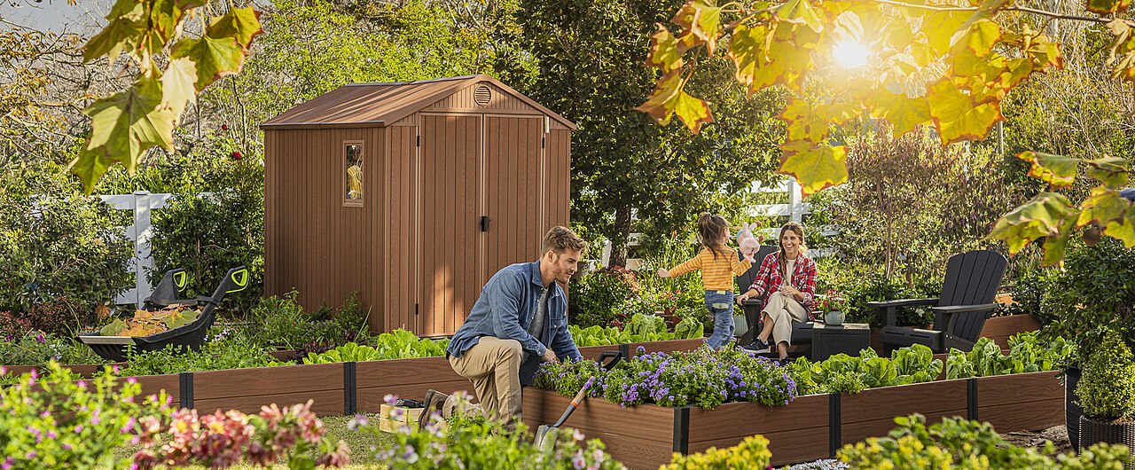 A backyard with a wooden shed, raised flowerbeds, a wheelbarrow and a fence