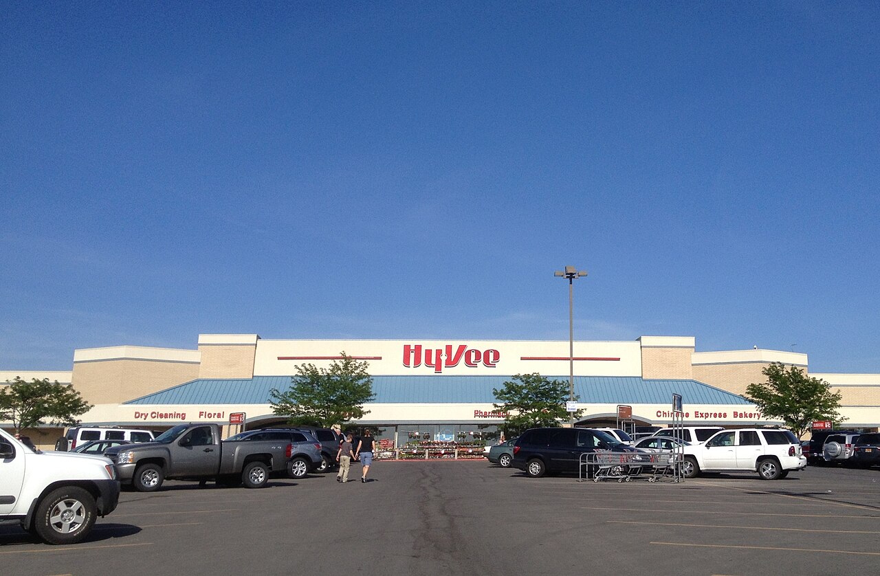 The front of an American grocery store (Hy-Vee), with shopping carts lined up and a parking lot