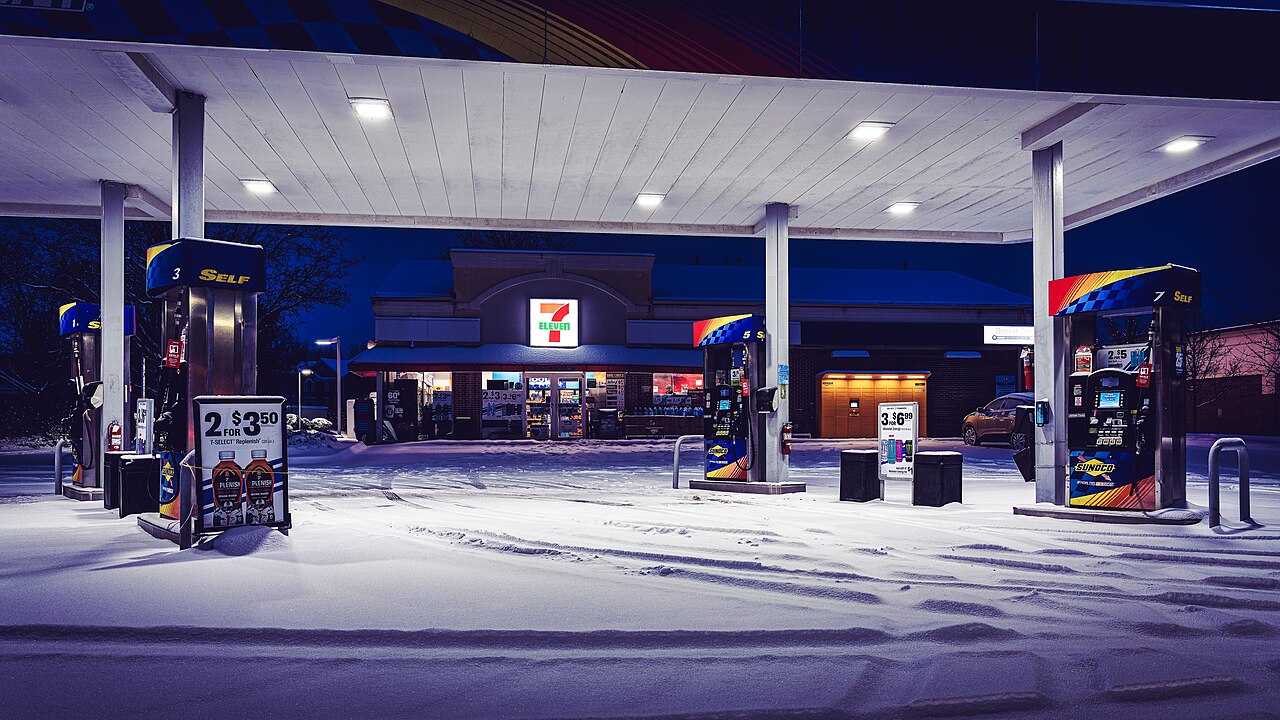 An American gas station at night, with fuel pumps under a lit canopy and a convenience store behind