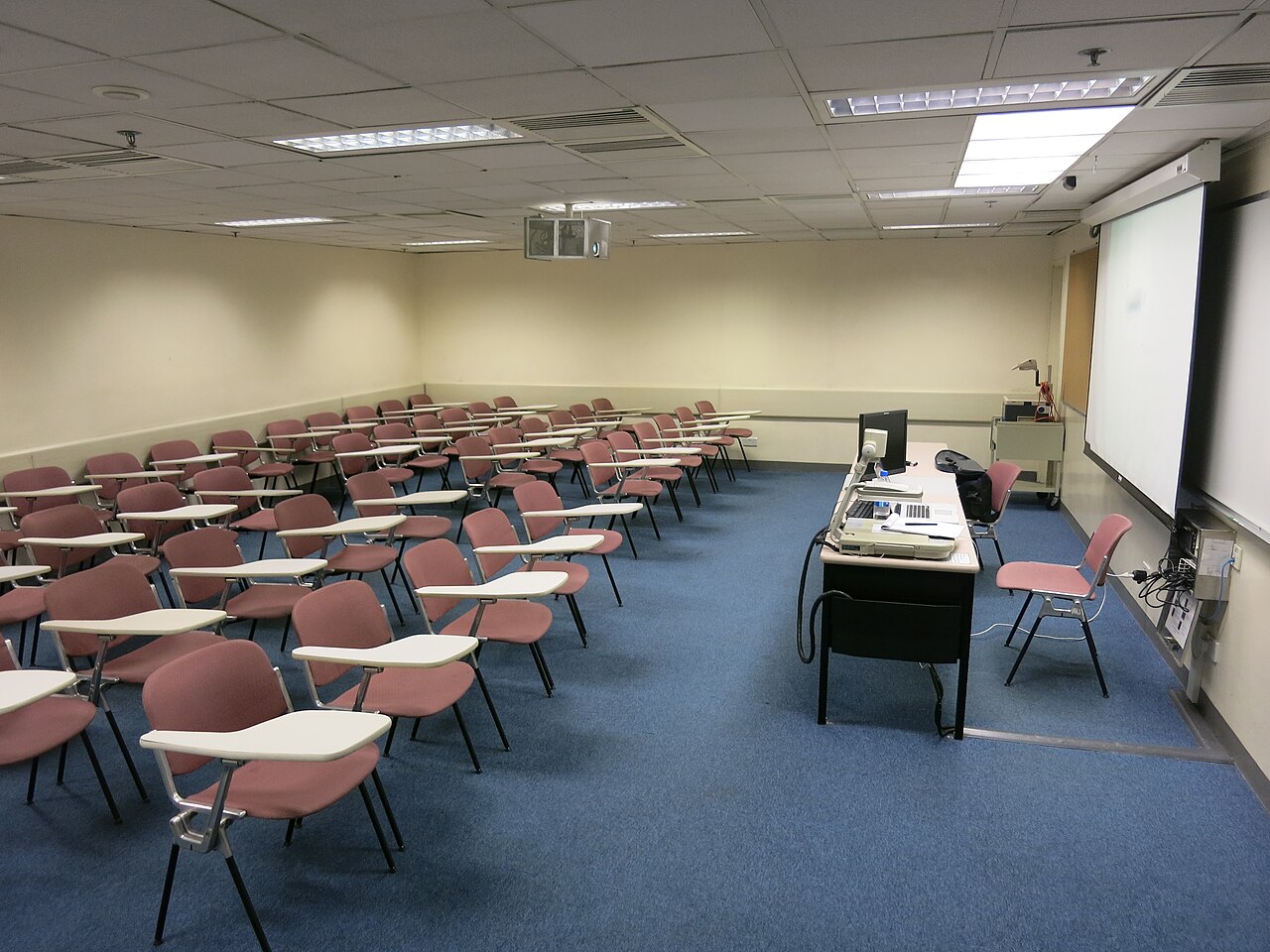 An empty classroom with rows of student chairs facing a teacher's desk