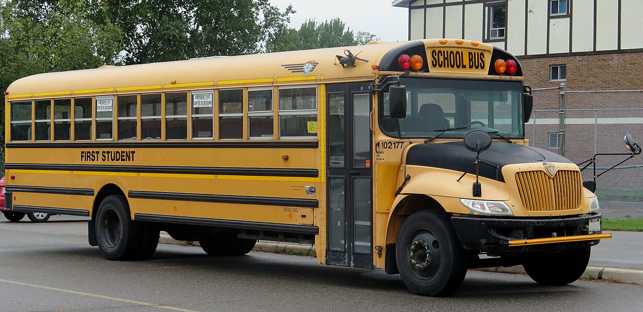 A yellow American school bus parked outside a school