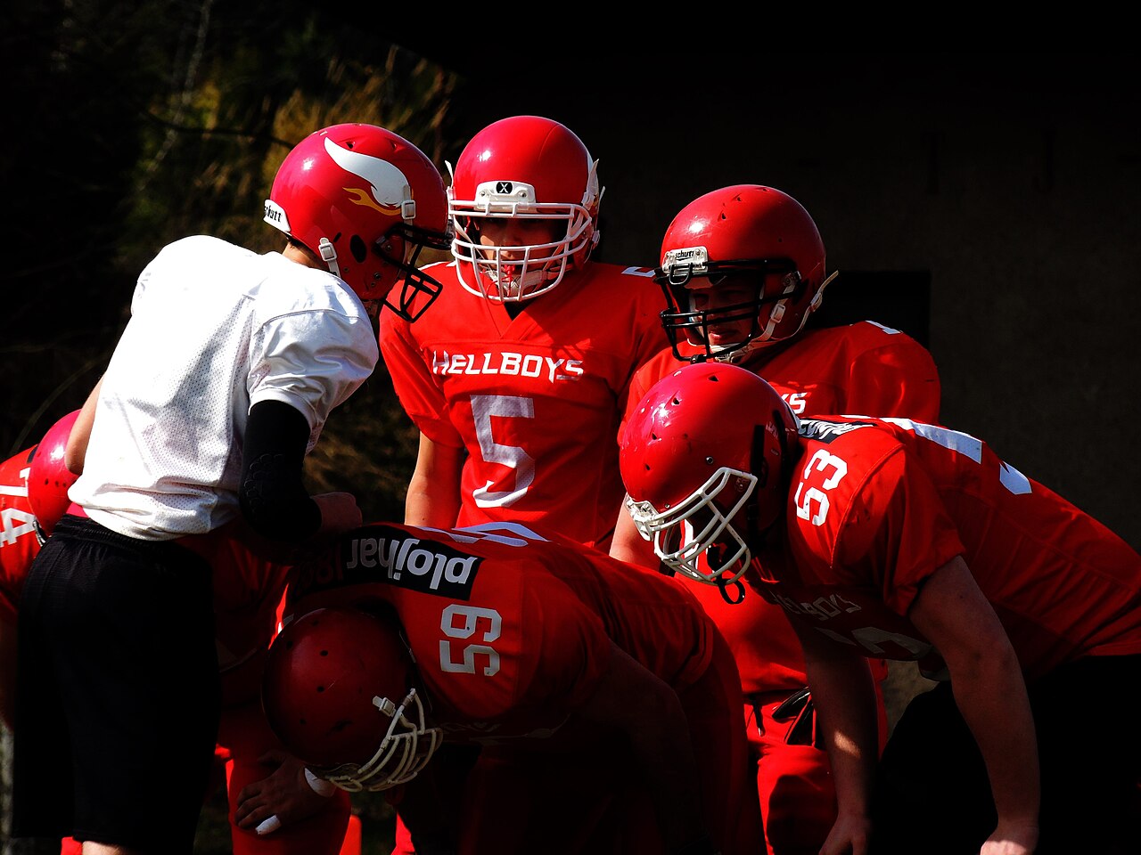 American football players in red jerseys and helmets gathered in a huddle
